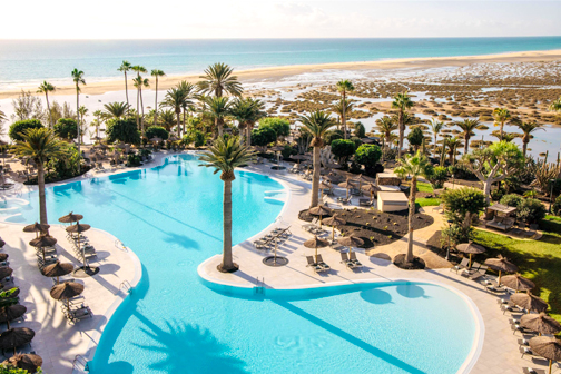 Groot lagunezwembad van Paradisus by Melia met palmbomen en ligbedden aan een zandstrand, met uitzicht op zee onder een heldere hemel.